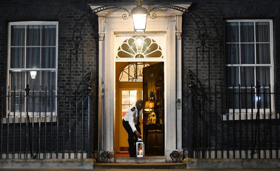 A custodian places a lit candle outside 10 Downing Street to mark one year of Covid-19 and to honour those who lost their lives to Covid-19 in London 23 March 2021